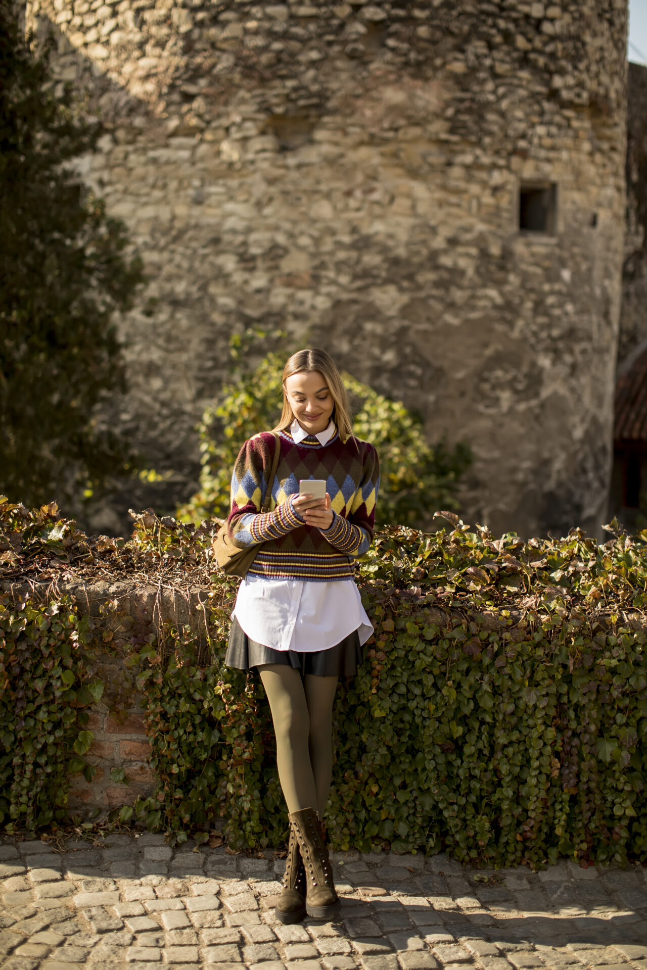 Pretty young woman standing with mobile phone on street at autum